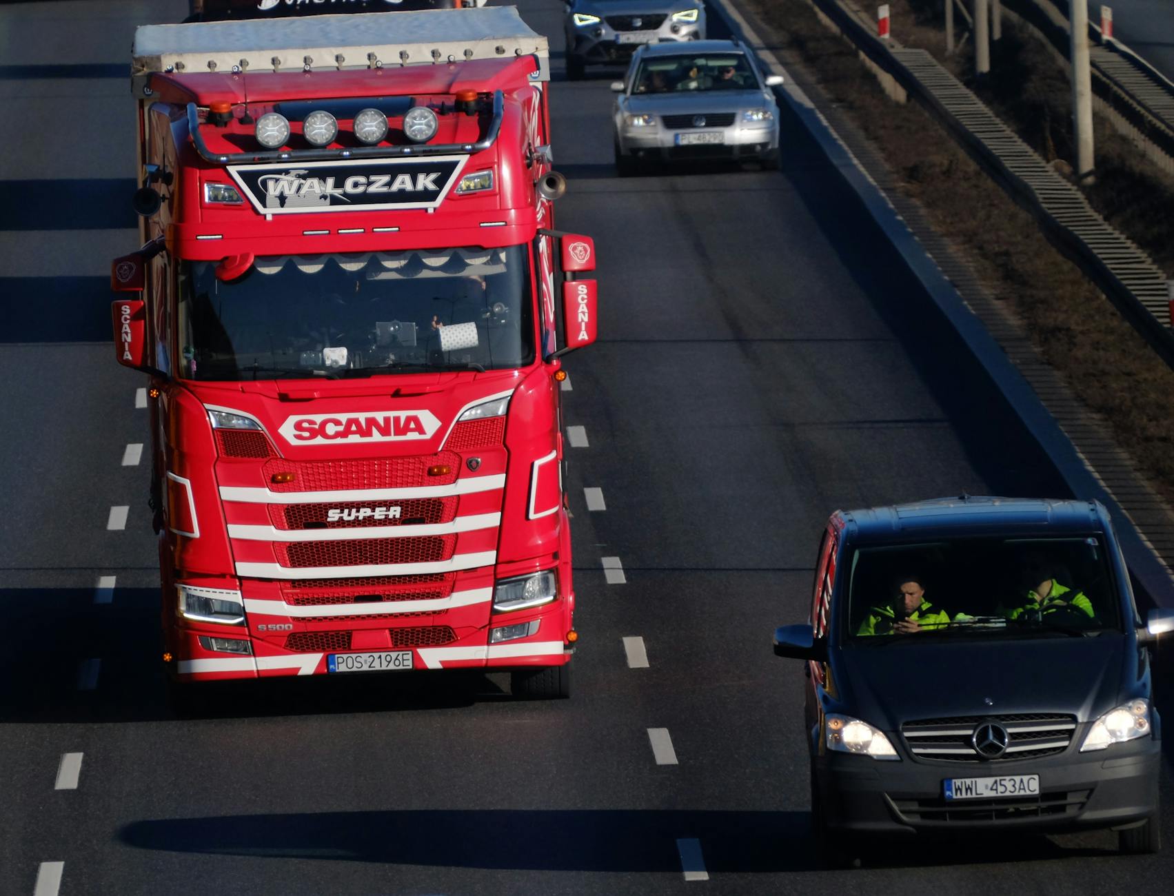 A red Scania truck driving on a highway with other vehicles, captured from above.