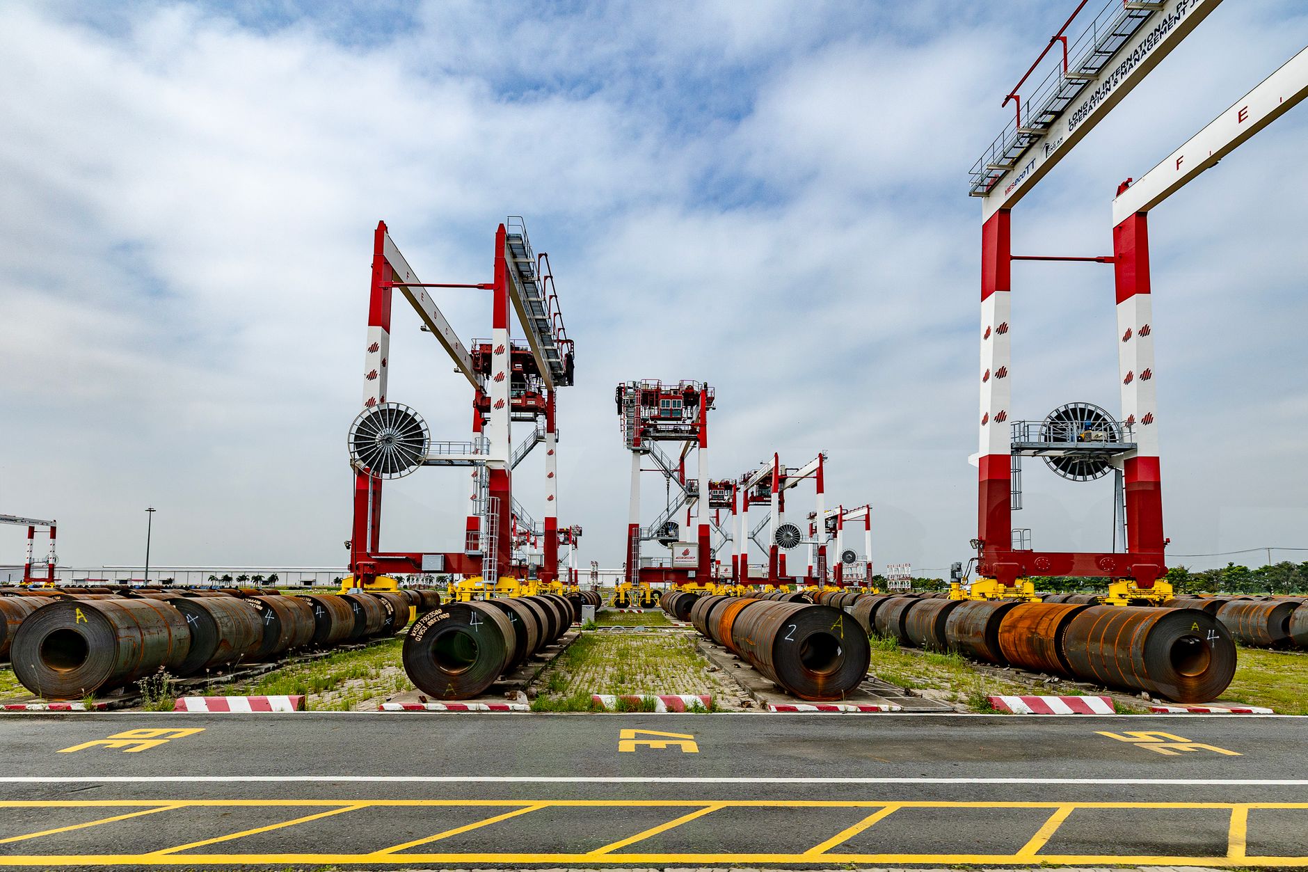 View of a shipping yard with heavy machinery and industrial pipes under a cloudy sky.