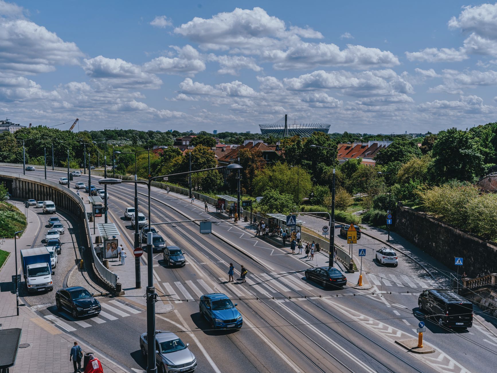 An aerial view showcasing Warsaw's city streets with a distant view of the National Stadium under a clear blue sky.