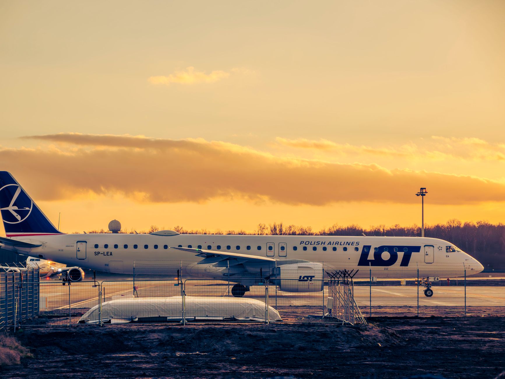 A LOT Polish Airlines plane on the tarmac at Wrocław Airport during a beautiful sunset.