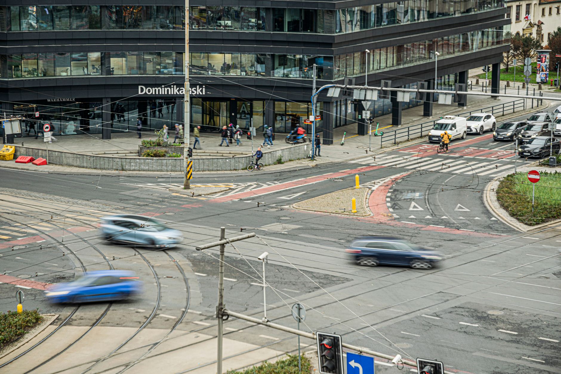 A bustling city intersection near a modern office building with blurred traffic and pedestrians.