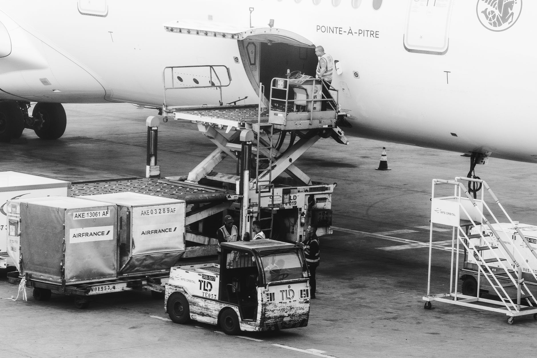 Black and white image of cargo being loaded on an airplane at an airport.