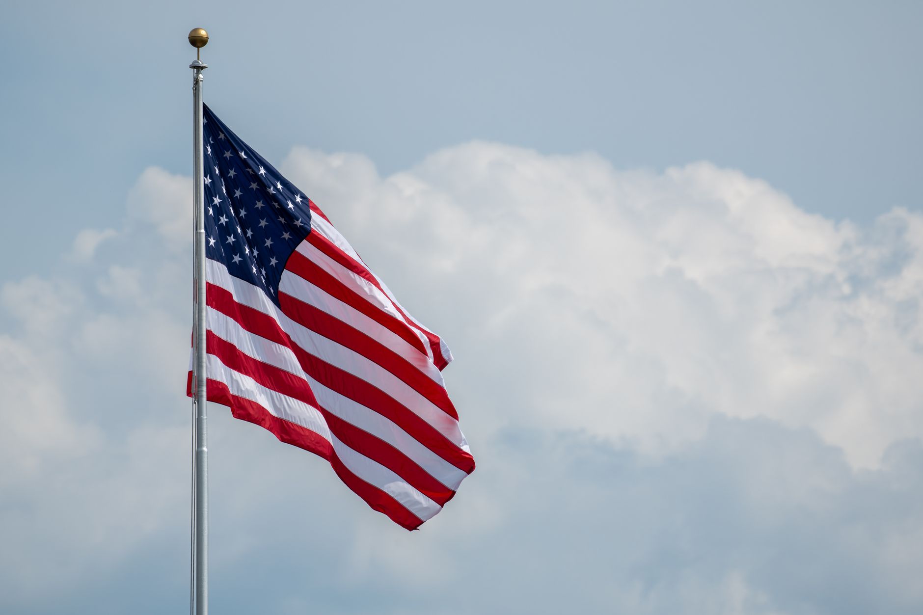 A vibrant American flag waving on a flagpole with a cloudy sky backdrop, symbolizing national pride.
