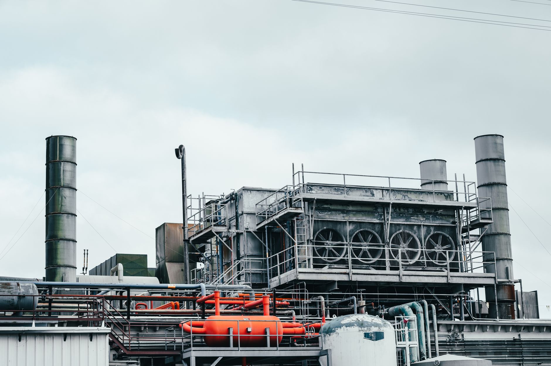 Industrial factory with metal pipes and special equipment surrounded with fences located against cloudy sky on street with power lines in to