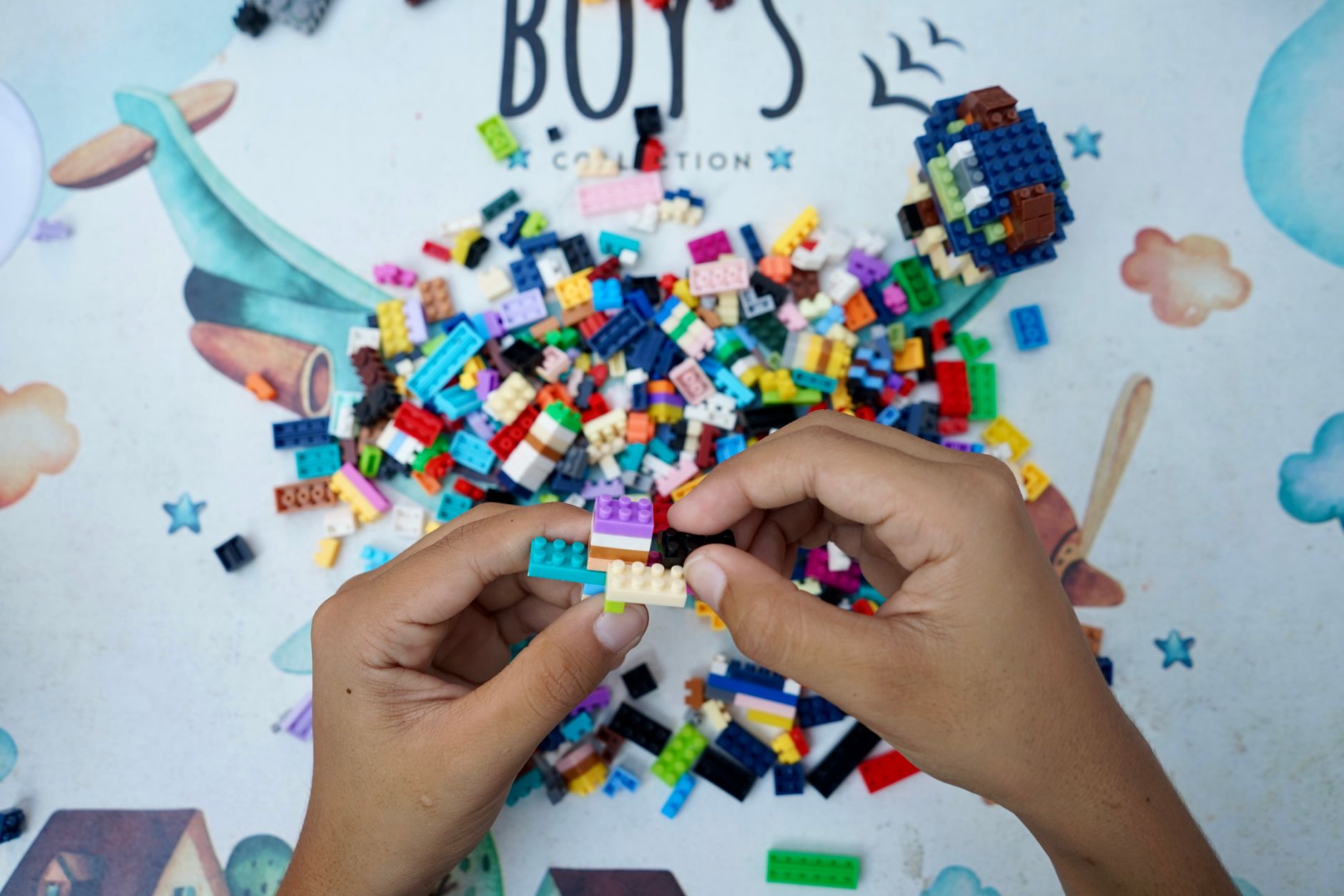 Hands of a child assembling colorful Lego bricks on an outdoor table, showcasing creativity and playfulness.