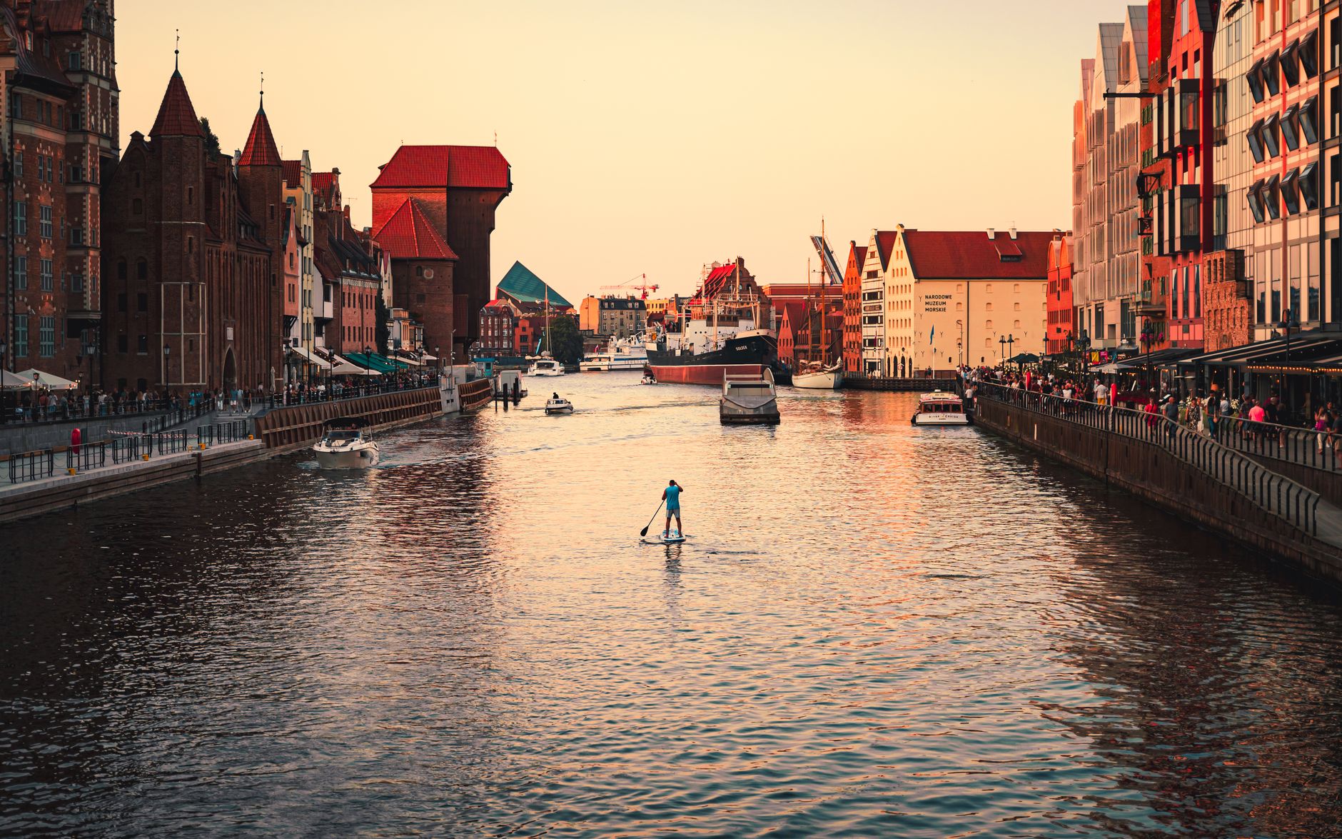 Beautiful sunset over Gdansk's canal with historic architecture and paddleboarding.