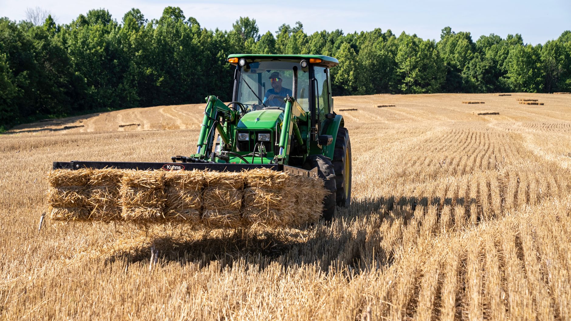 A farmer operates a tractor loading hay bales in a sunny North Carolina field.