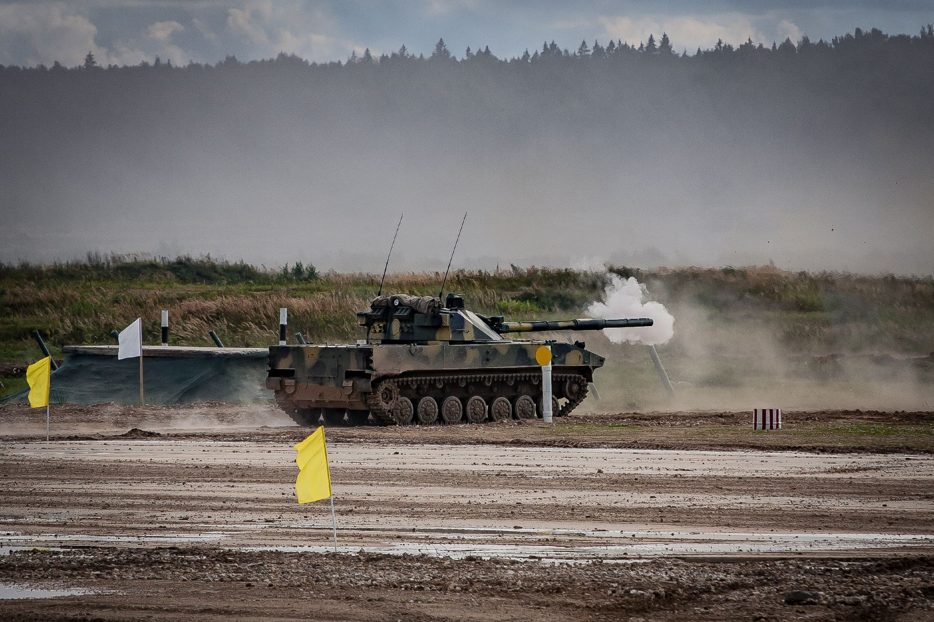 A military tank firing a shell during training in an open field.