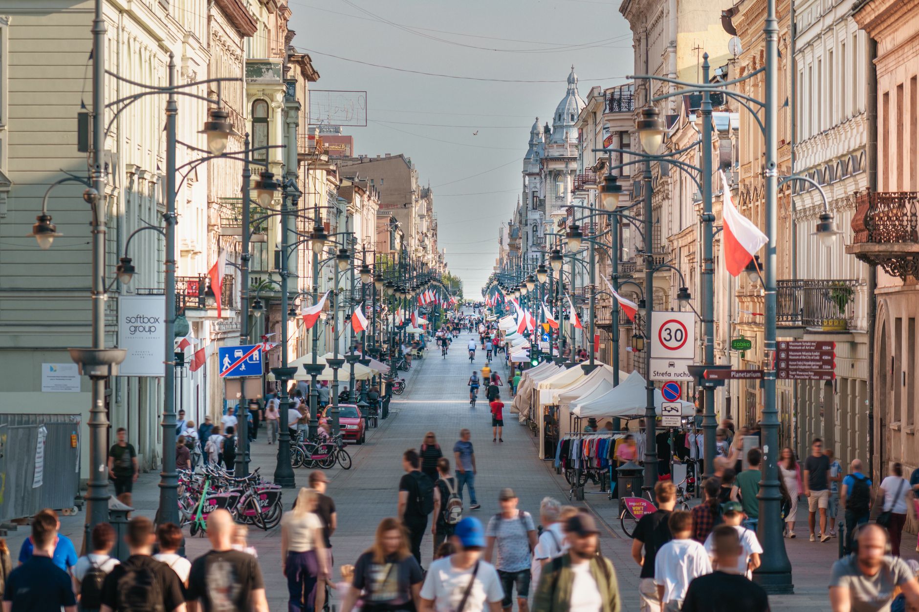 Busy scene on Piotrkowska Street, Łódź with flags and people walking. A vibrant cityscape showcasing Polish culture.