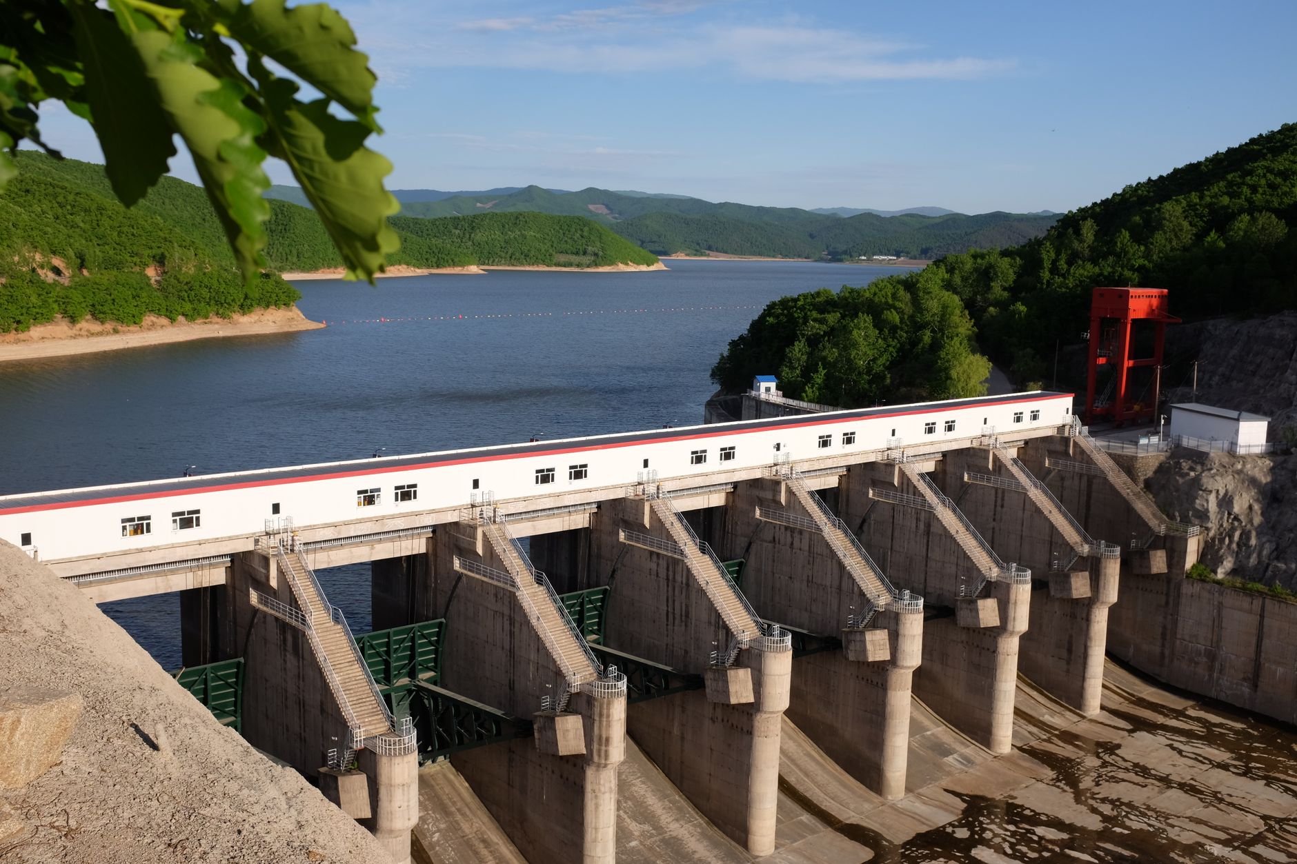 Aerial view of a large hydroelectric dam surrounded by lush forests and a clear blue lake.