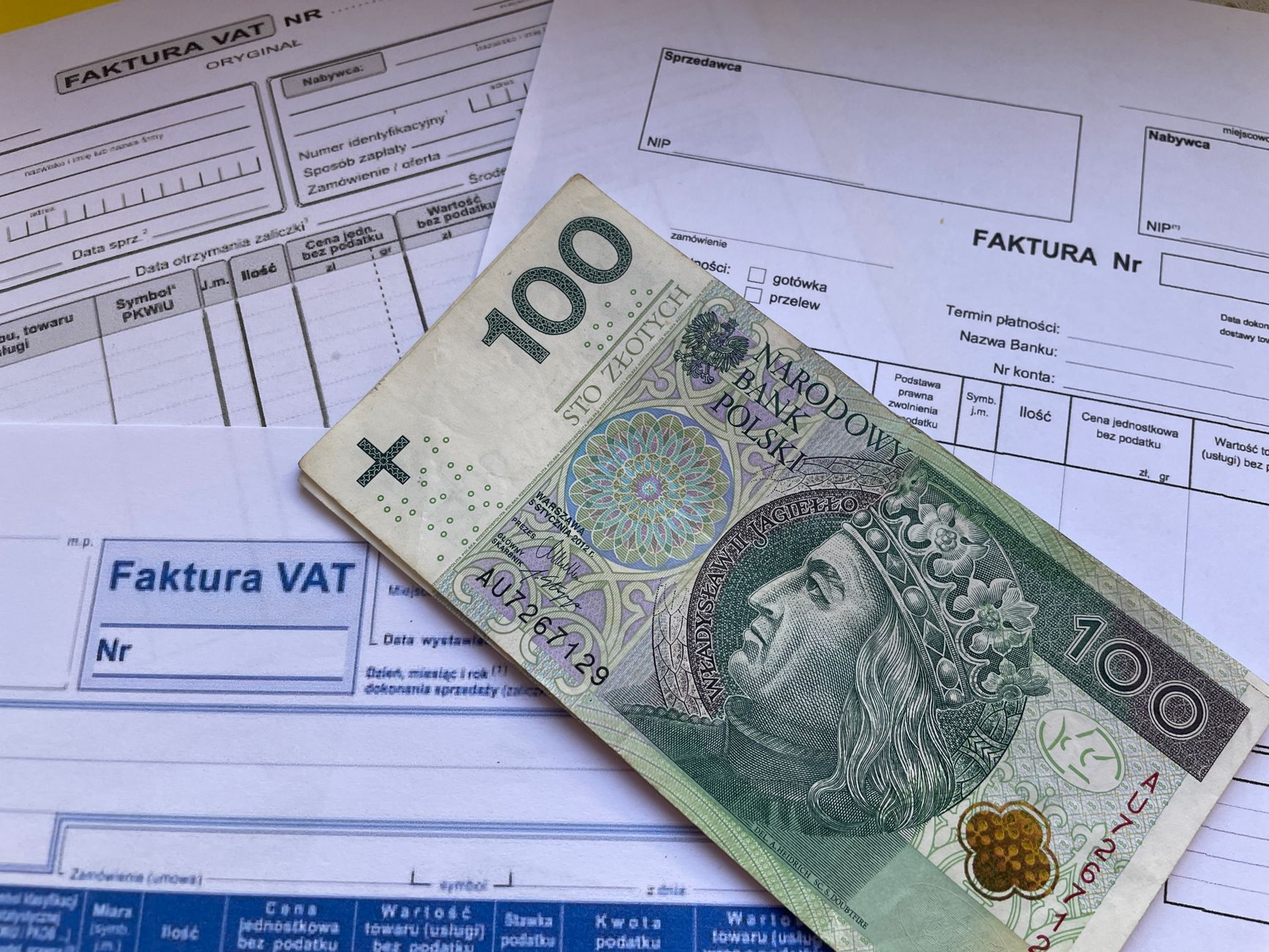 A 100 Polish Zloty note placed on top of business VAT invoices, symbolizing finance and economics.