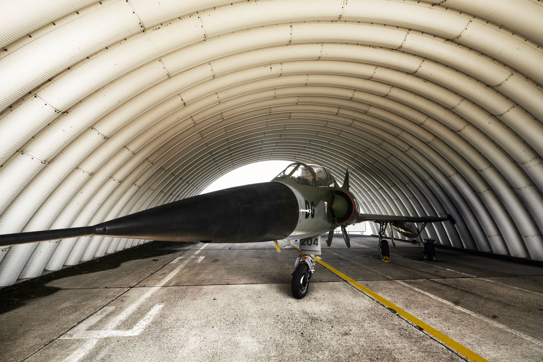 A fighter jet parked inside an arched military hangar, showcasing its sleek design.