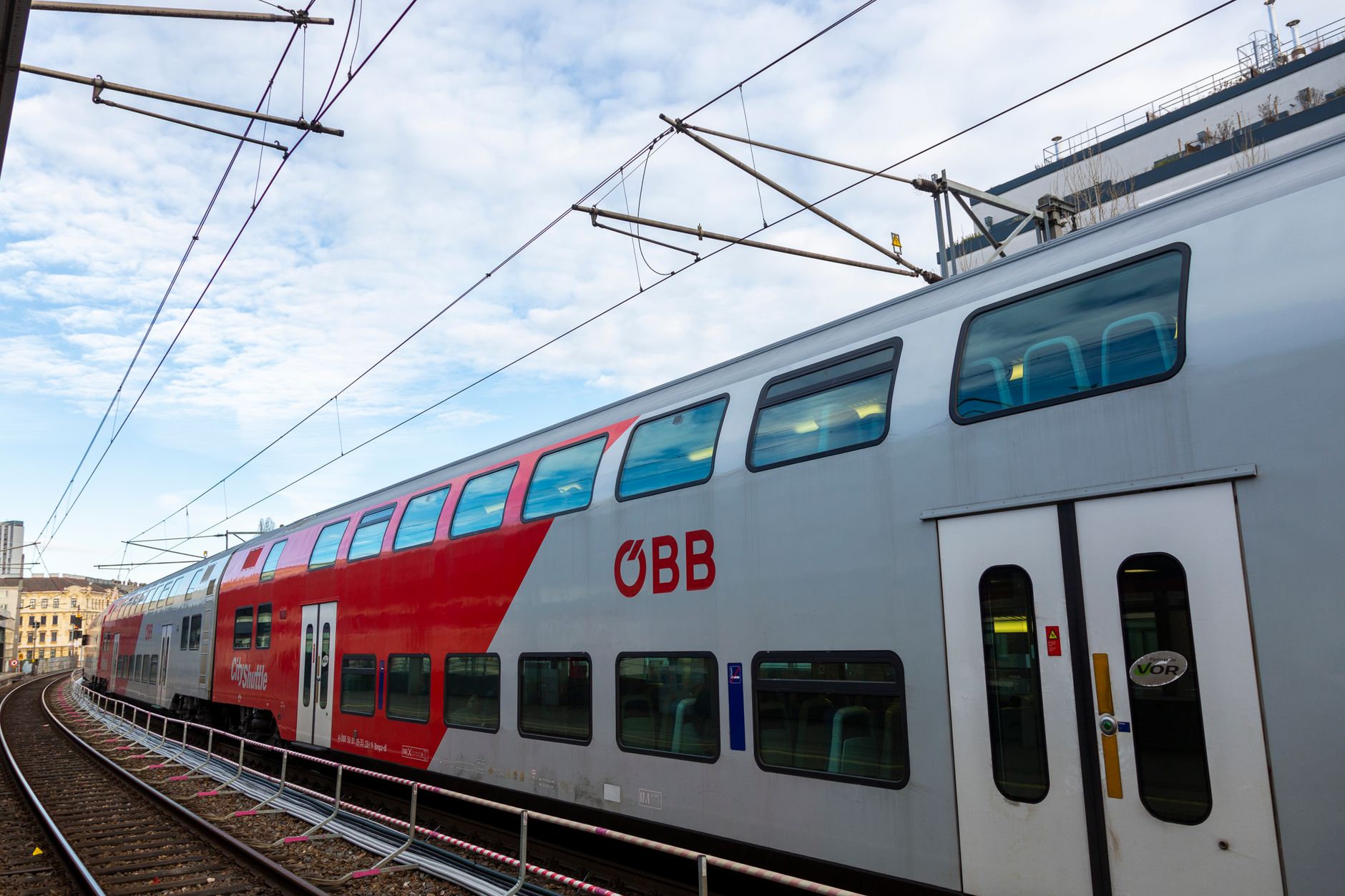 A sleek ÖBB double-decker train stopped at a European railway station platform on a clear day.
