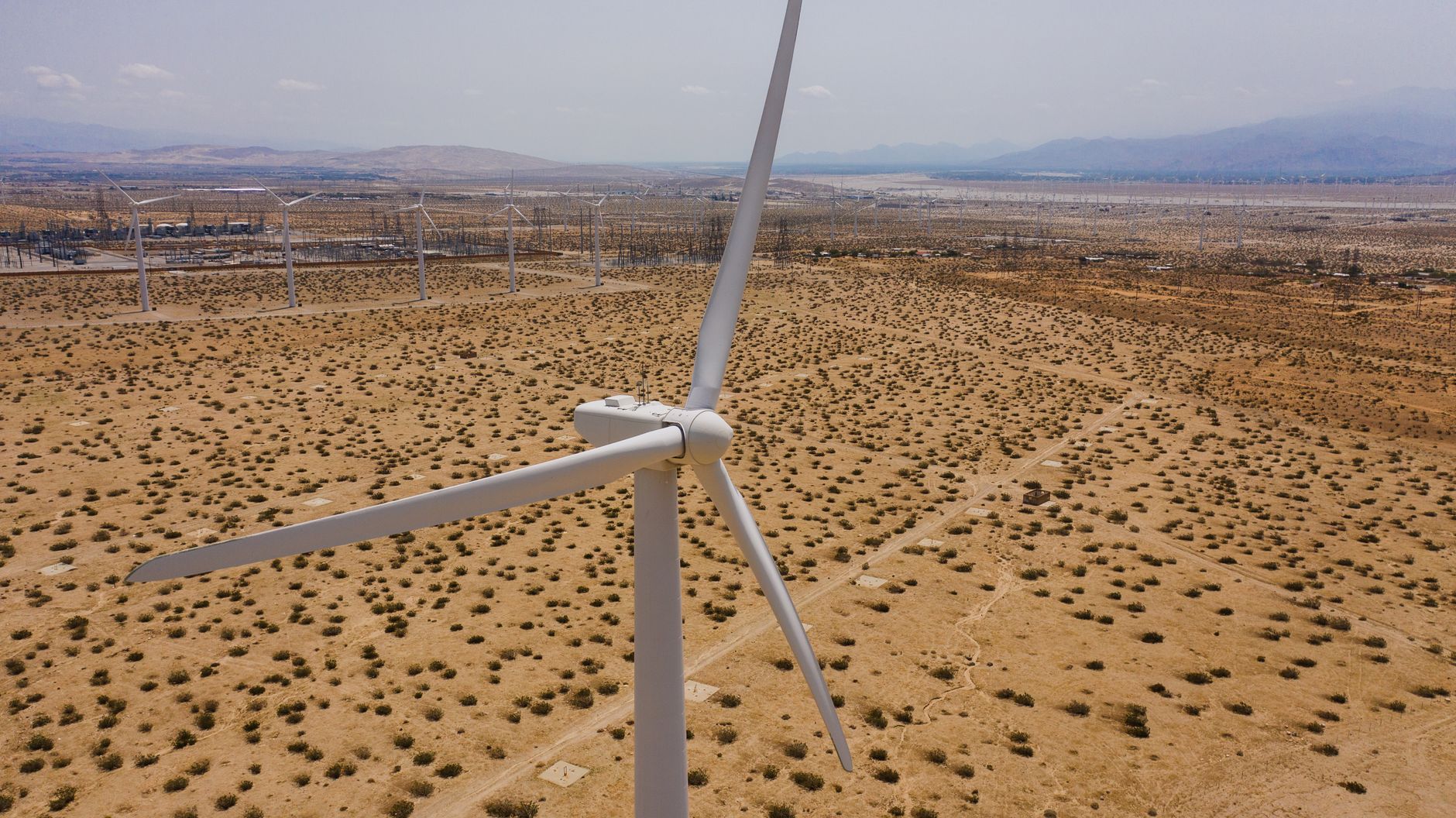 A panoramic aerial shot showcasing wind turbines amid a vast desert landscape under a clear sky.