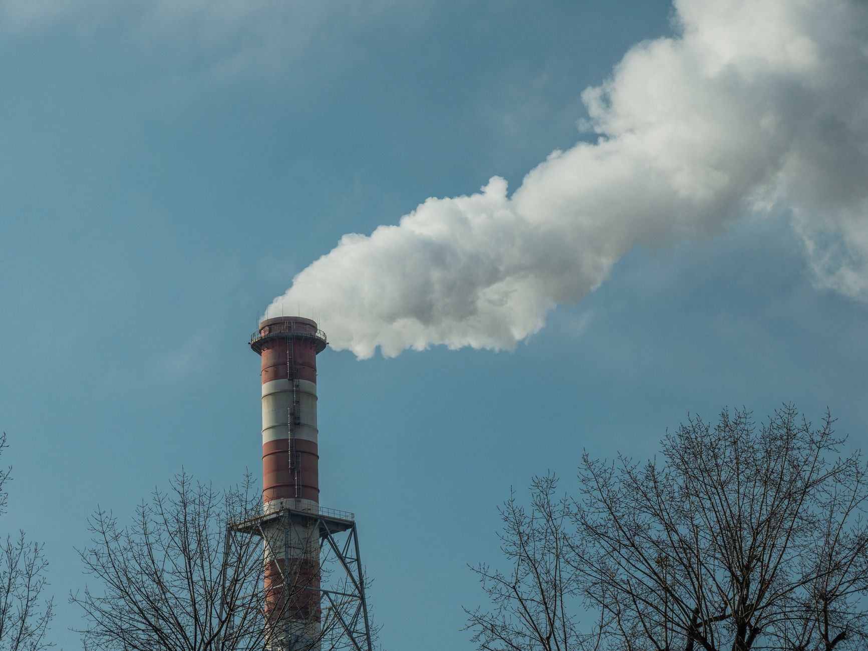 A red industrial chimney releases smoke against a clear blue sky in Wrocław.