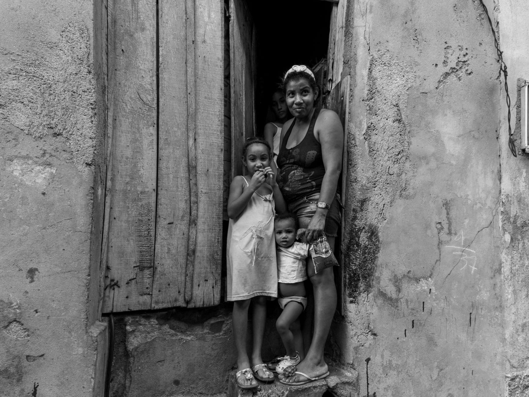 Black and white portrait of a family standing in a rustic doorway, evoking emotion and authenticity.