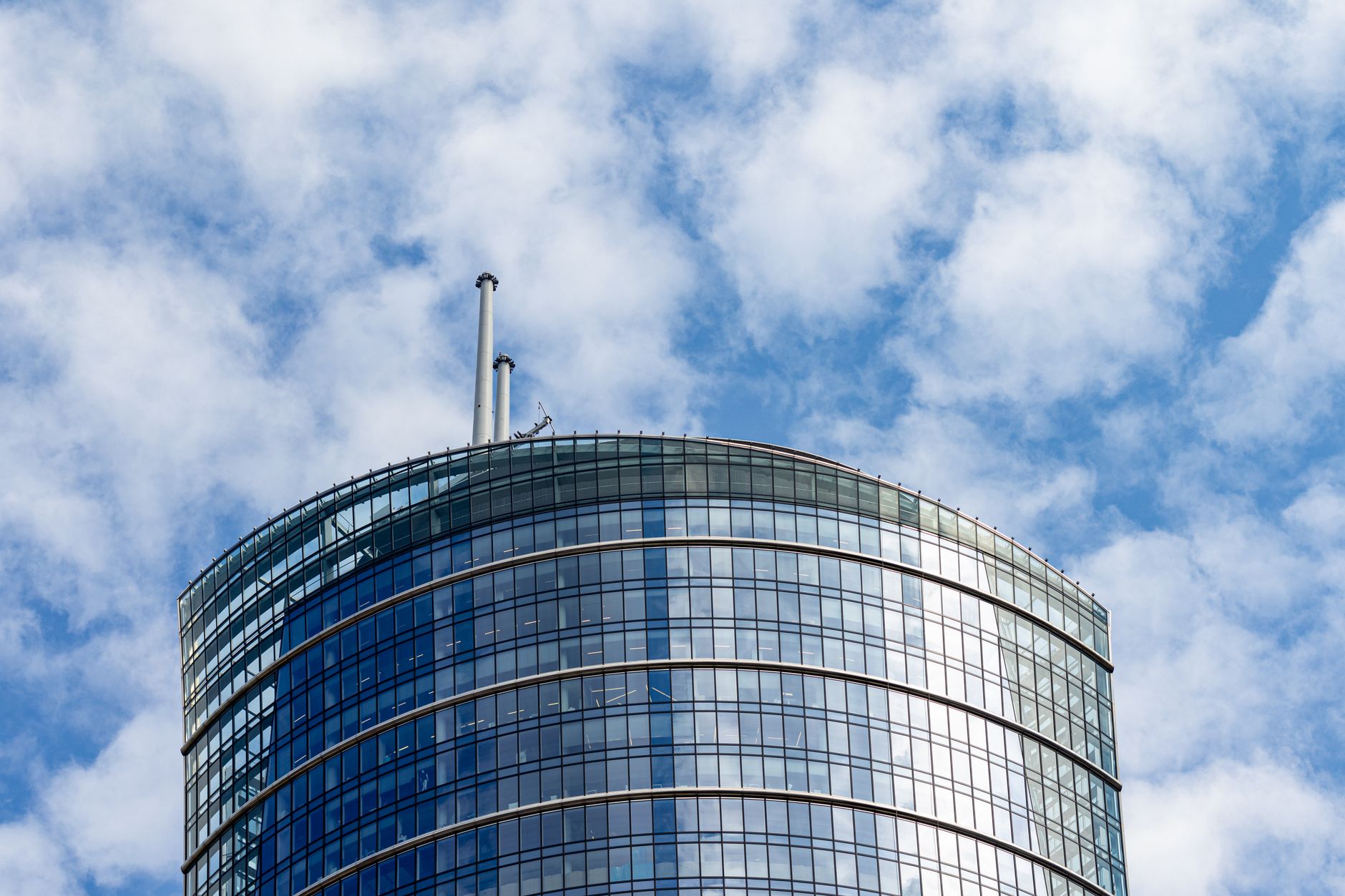 View of a modern glass skyscraper in Warsaw, Poland, with a vibrant blue sky and clouds backdrop.