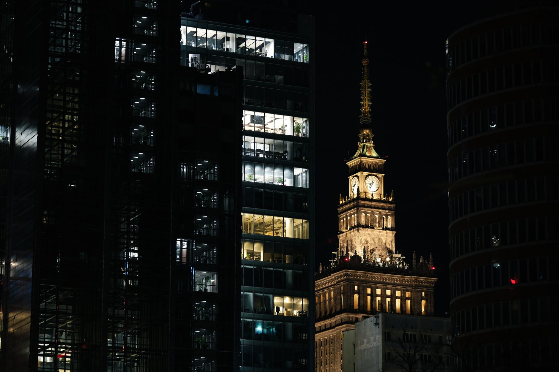 Nighttime view of Warsaw's Palace of Culture with modern skyscrapers, showcasing vibrant city life.